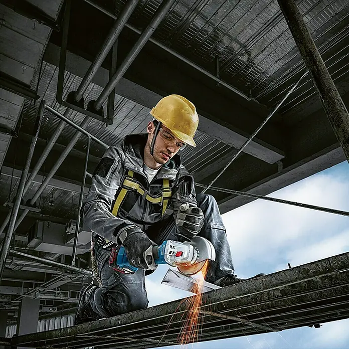 Bosch Professional AMPShare 18V Akku-Winkelschleifer GWS 18V-7 - 18 V, Ohne Akku, Durchmesser Scheibe: 125 mm - Mann mit gelbem Helm benutzt einen Bosch Winkelschleifer mit Funkenflug auf einem Gerüst.