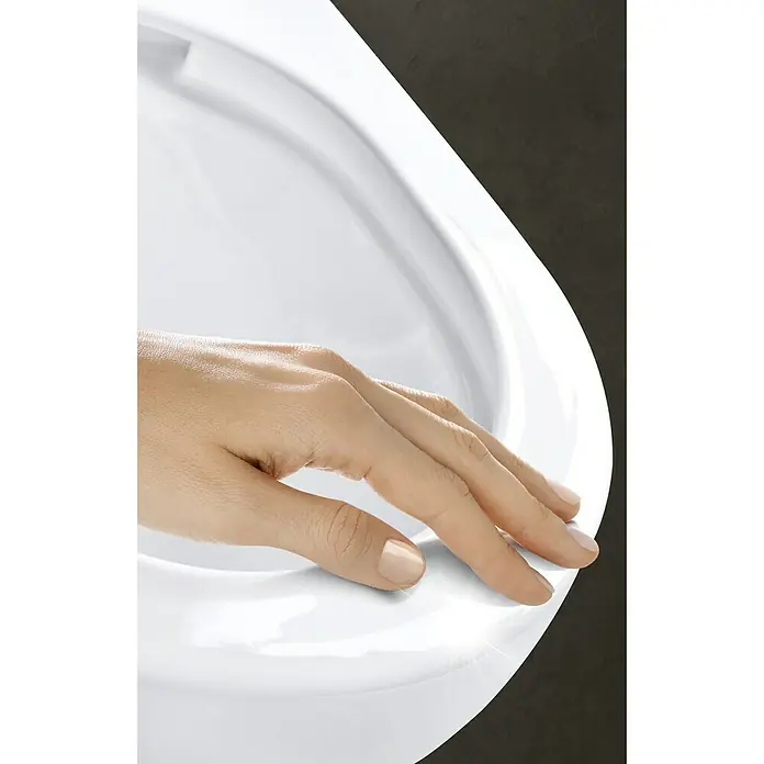 Grohe Sensia Arena Wand-Dusch-WC-Set - Spülrandlos, Mit antibakterieller Glasur, Spülform: Tief, WC Abgang: Waagerecht, Weiß - Nahaufnahme einer Hand, die die makellose Oberfläche einer weißen Keramiktoilette berührt, was Reinheit und Hygiene vermittelt.