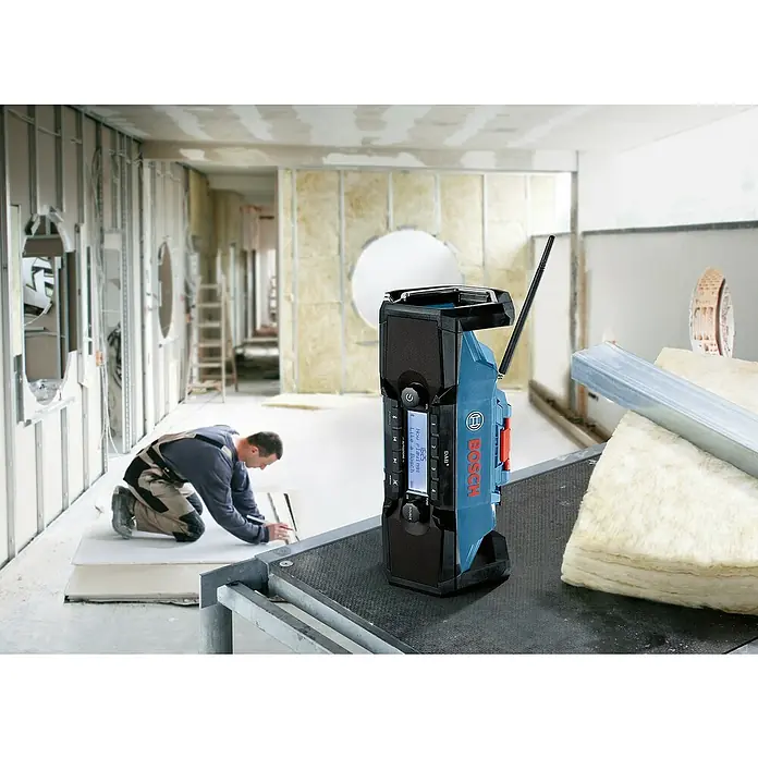 Bosch Professional AMPShare 18V Akku-Baustellenradio GPB 18V-2 SC - 18 V, Ohne Akku, Frequenz: 87,5 - 108 MHz (UKW/FM) - Baustellenradio von Bosch in Blau und Schwarz. Ein Bauarbeiter arbeitet im Hintergrund.