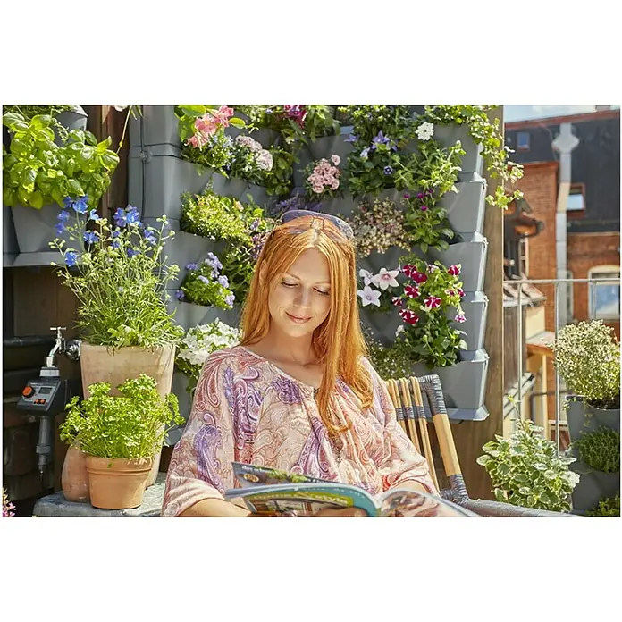 Gardena Bewässerungs-Set NatureUp! Vertikal Wasserhahn - Passend für: Bewässerung von bis zu 27 Pflanzen/9 vertikalen Pflanzbehältern - Die Frau entspannt sich im Garten auf dem Balkon mit vertikalen Pflanzgefäßen und liest eine Zeitschrift.