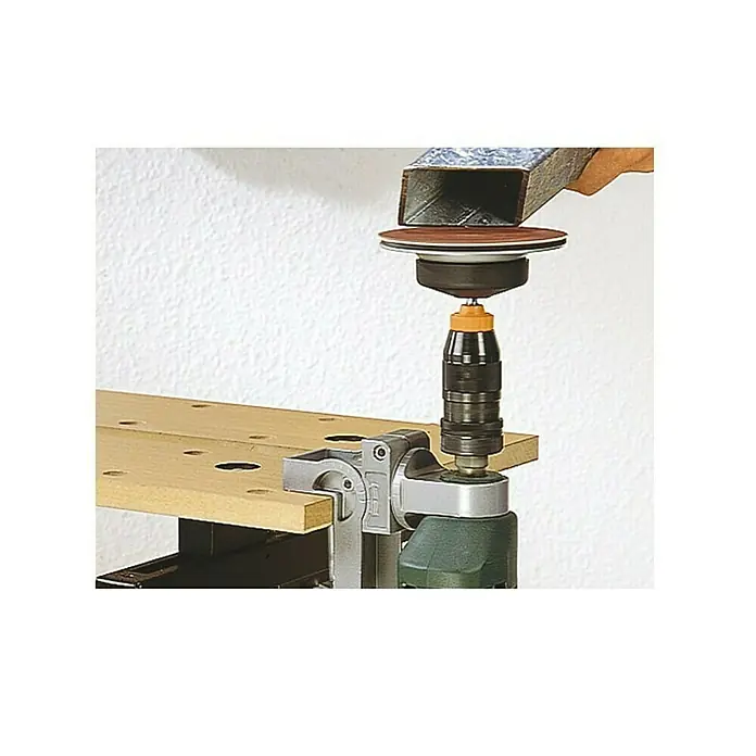Wolfcraft Soporte de taladro - Apertura máxima: 60 mm - Se muestra un taladro de columna con un disco de lijado conectado, listo para lijar una pieza de trabajo de metal, que se sujeta con una mano.