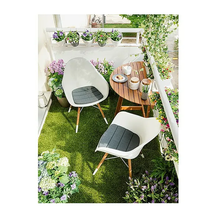 Sunfun Diana Mesa de balcón - L x An x Al: 100 x 50 x 75 cm, Acacia, Abatible, Curvado, Marrón natural - Balcón relajante con dos sillas blancas con cojines grises y una mesa redonda de madera, decorado con flores.