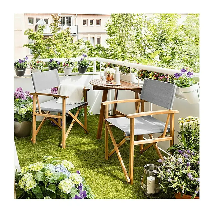 Sunfun Diana Mesa de balcón - L x An x Al: 100 x 50 x 75 cm, Acacia, Abatible, Curvado, Marrón natural - Acogedor balcón con dos sillas plegables grises, una mesa de madera y muchas plantas que crean un ambiente acogedor.
