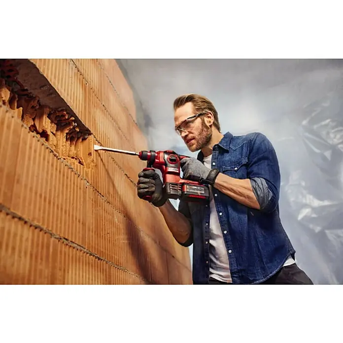 Einhell Professional PXC 18V Martillo combinado de batería Herocco - 18 V, Sin batería, 0 Ah, 2,2 J - Un hombre utiliza un martillo perforador inalámbrico Einhell en una pared de ladrillos, usando gafas de seguridad y guantes.