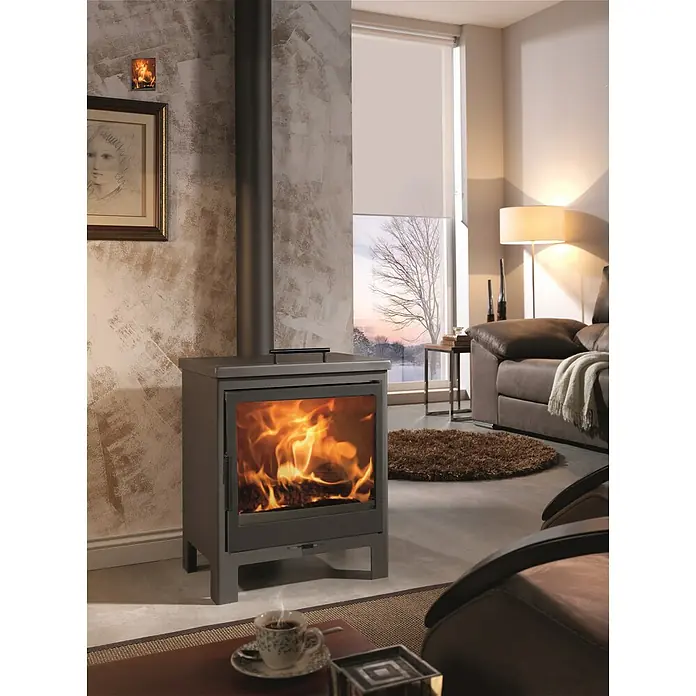 Panadero Estufa de leña Newport - 8 kW, Volumen de calefacción: 180 m³, Negro - Una acogedora sala de estar con una estufa de leña moderna que irradia calidez y ambiente. Las llamas bailan dentro, creando un ambiente confortable.