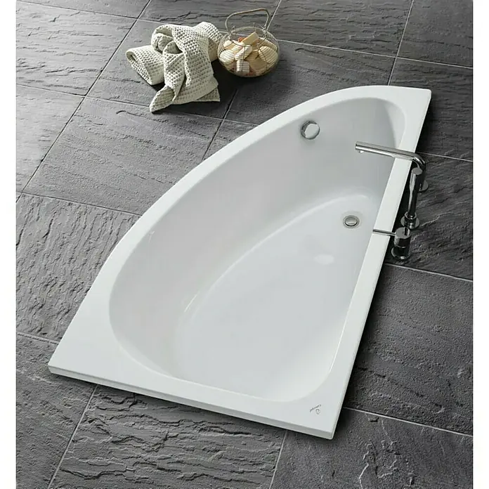Camargue Eckbadewanne Houston - L x B: 160 x 95 cm, Sanitäracryl, Weiß, Links - Ein weißes, trapezförmiges Badezimmer mit Armatur, das auf dunklen Steinfliesen steht, daneben ein Handtuch und eine Schale mit Seifen.