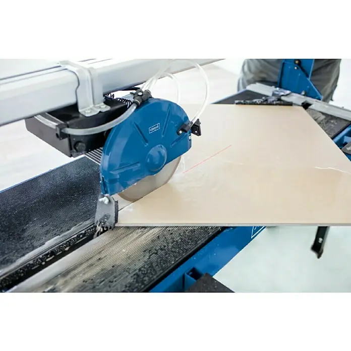 Scheppach Elektro-Fliesenschneider FS 4700 - 1.200 W, Max. Schnittlänge: 1.200 mm, Schnitttiefe bei 90 °: 34 mm - Nahaufnahme einer Fliesensäge beim Schneiden einer Fliese. Das Gerät ist blau und silber, der Schnitt ist präzise.