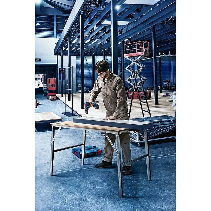 Bosch Professional AMPShare 18V Akku & Ladegerät - 18 V, 1 Akku, 4 Ah - Ein Handwerker bohrt mit einer Bosch Akku-Bohrmaschine ein Werkstück auf einem Arbeitstisch in einer Werkshalle.