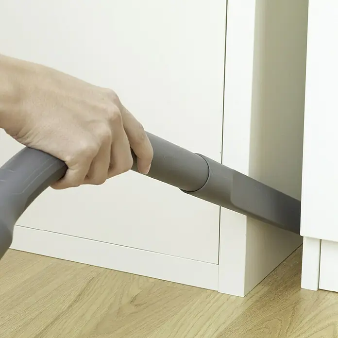 Thomas Waschsauger Aqua+ Pet & Family - 1.600 W, Behältervolumen: 1,8 l - Die Person hält einen Staubsauger, um den Staub zwischen den Möbeln unter dem Schrank in einem Wohnzimmer zu saugen.