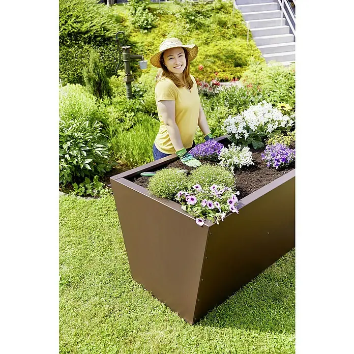 Gutta Hochbeet Valenta 200 - 200 x 90 x 80 cm, Aluminium, Rost Matt - Frau gärtnert in einem modernen, hohen Pflanzgefäß im Garten, das mit bunten Blumen bepflanzt ist.