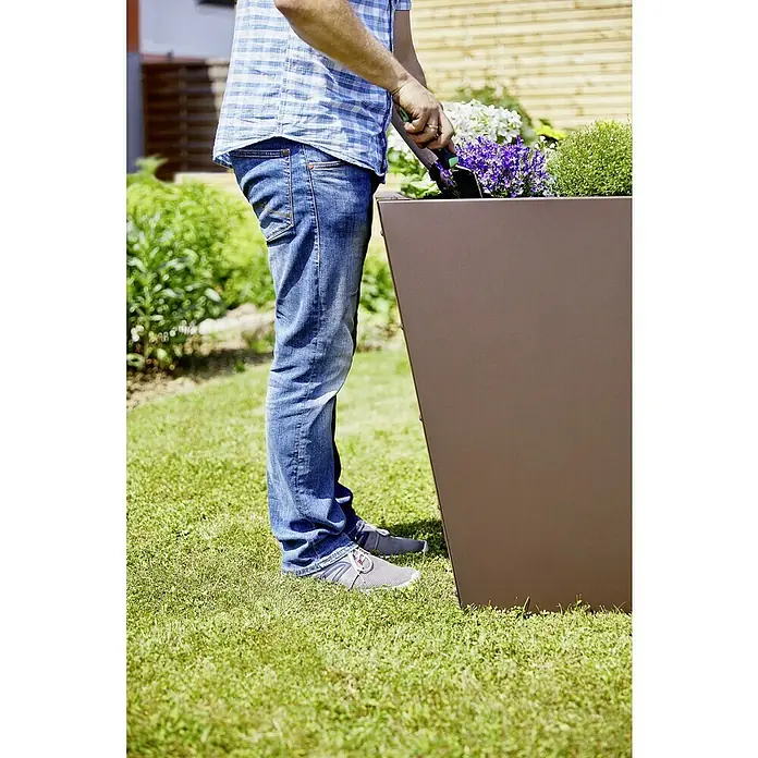Gutta Hochbeet Valenta 200 - 200 x 90 x 80 cm, Aluminium, Rost Matt - Eine Person, die draußen in einem hohen, kastenförmigen Pflanzgefäß Blumen pflanzt.