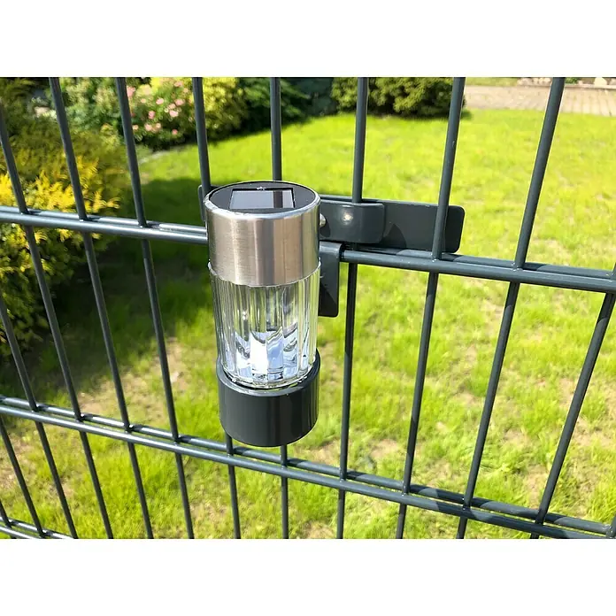 WMT Eindrehhalterung für Solarlampen - Passend für: Stabgitterzäune & Doppelstabmatten, Zäune - Nahaufnahme einer Solarleuchte, die an einem Zaun befestigt ist, mit einem klaren, gerippten Lampenschirm und einem silbernen Oberteil.