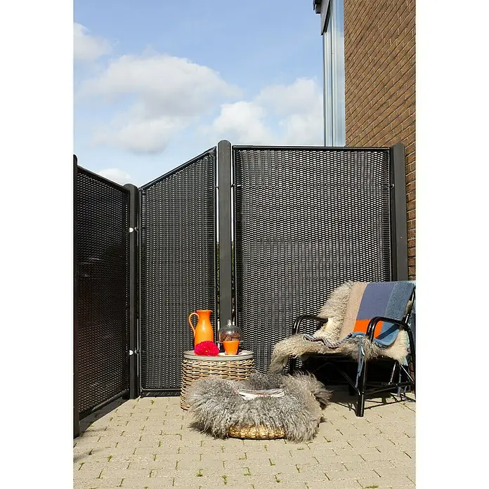 Plus Sichtschutzelement Trend - 55 x 140 cm, Kunststoff, Schwarz - Eine Szene im Freien mit einem dekorativen Raumteiler, einem Rattansessel mit Fell und einer Beistelltischgruppe mit orangefarbenen Akzenten.