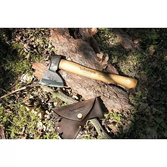 Jägerbeil-Set - 500 g, 330 mm - Wisent Jägerbeil Axt mit Metallkopf, hellem Holzstiel und dunkelbrauner Lederscheide, auf Rinde und Waldboden liegend.