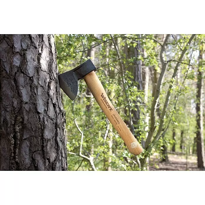 Jägerbeil-Set - 500 g, 330 mm - Eine Axt mit schwarzem Kopf und hellem Holzgriff steckt in einem Baumstamm im Wald.