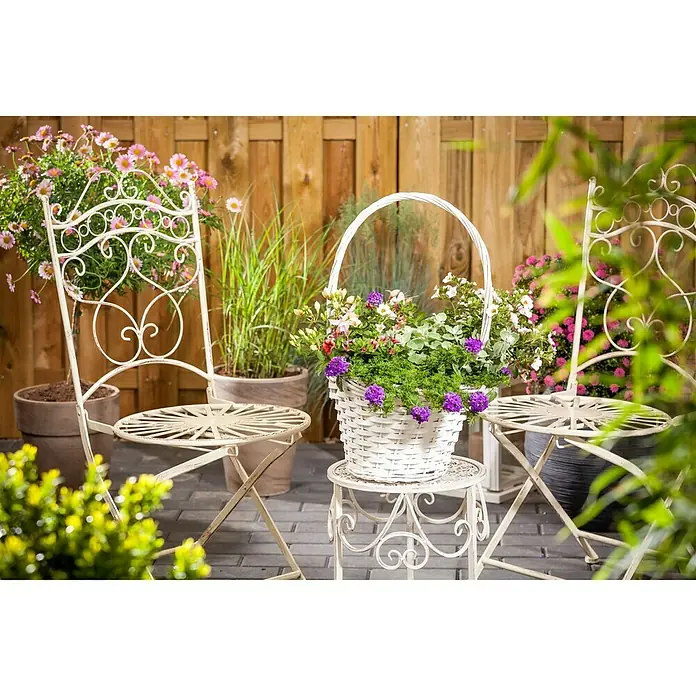 Piardino Verbena - Verbena Hybride, Tamaño de maceta: 13 cm, En función de la variedad - Imagen de dos sillas y una mesita con una cesta de flores, todo dispuesto al aire libre.