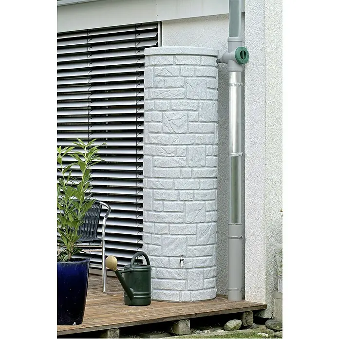 Arves Regenspeicher Arcado - 460 l, Granitfarben, 1 Stk. - Regenwassertank in Steinoptik neben einem Fallrohr auf einer Holzterrasse, ideal zur Gartenbewässerung. Praktisch und dekorativ.