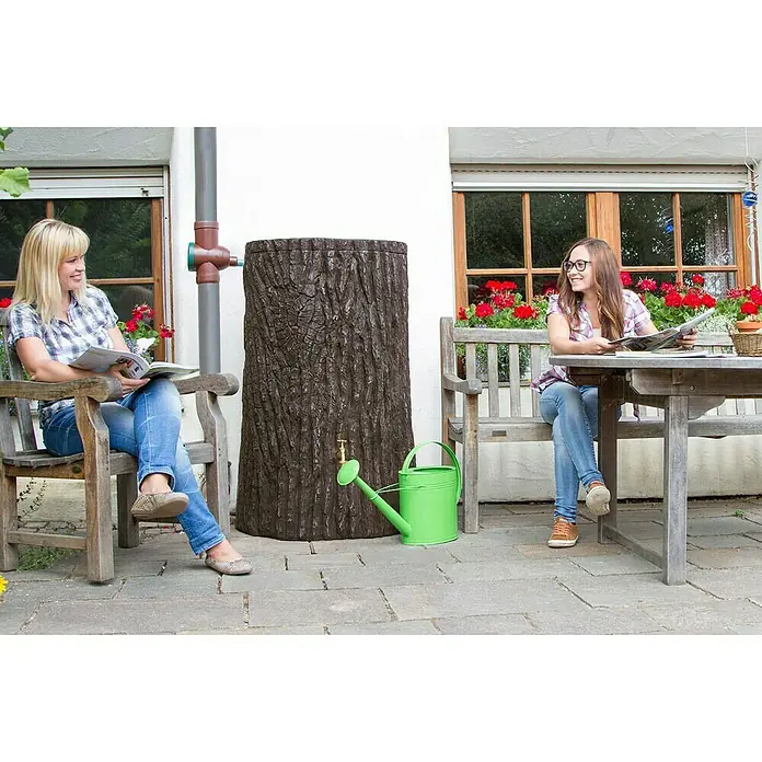 Arves Regenspeicher Evergreen - 475 l, Dunkelbraun, 1 Stk. - Zwei Frauen entspannen auf einer Terrasse neben einem dekorativen Regenwassertank in Baumstammoptik und einer grünen Gießkanne.