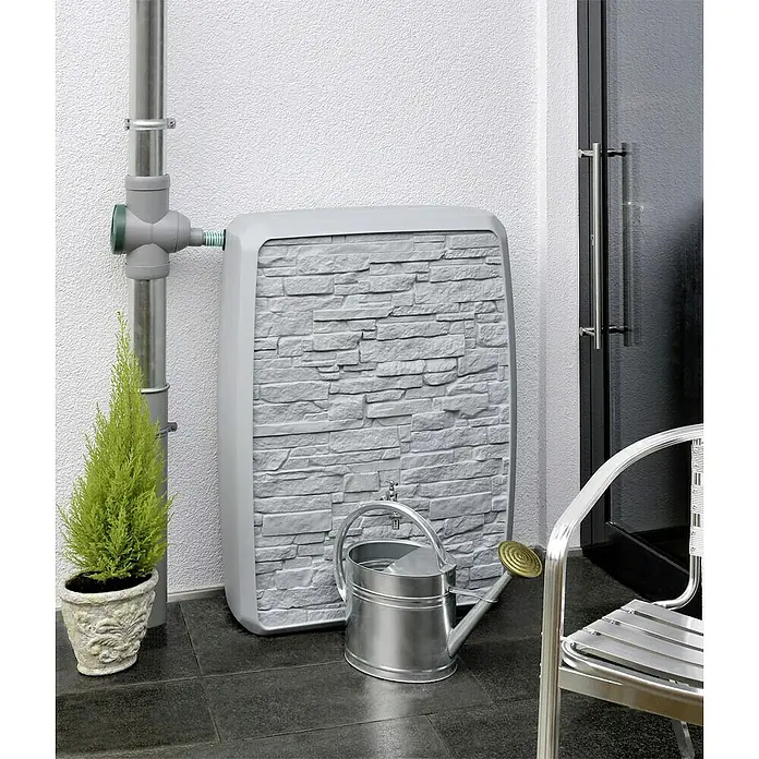 Arves Regenspeicher Multitank - 250 l, Grau - Die Regentonne in Steinoptik ist eine stilvolle und praktische Lösung zur Wassergewinnung im Garten. Eine Gießkanne steht davor.