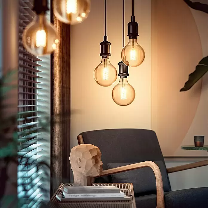 Philips Hue Bombilla LED inteligente Globo gigante - E27, Intensidad regulable, Blanco cálido, 550 lm, 7 W, Denominación de la lámpara: G125 - Bombillas de filamento Philips Hue de color ámbar cálido cuelgan como iluminación decorativa en una sala de estar acogedora, iluminando un sillón oscuro y detalles de madera.