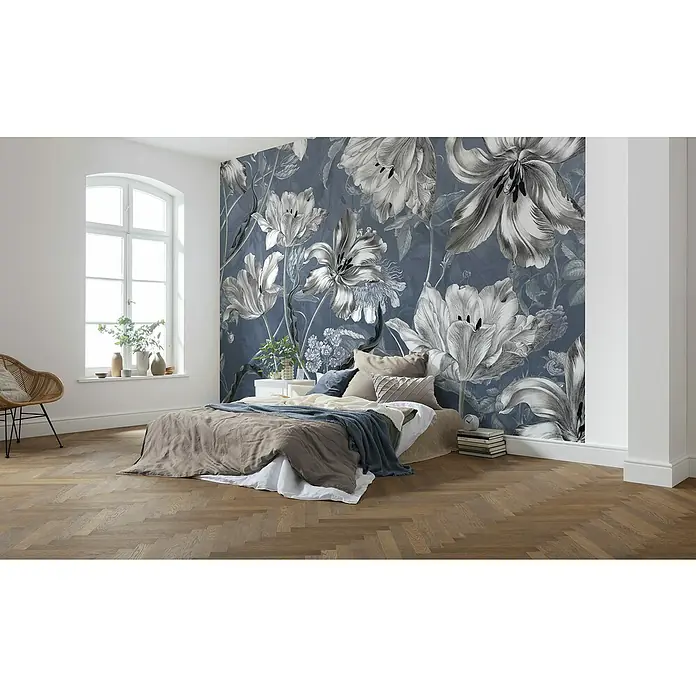 Komar Fototapete Merian Blue - 7 -tlg., B x H: 350 x 250 cm, Vlies - Schlafzimmer mit einer Wandtapete mit Blumenmuster in Grau- und Blautönen. Das Zimmer ist mit einem Bett und einem Sessel ausgestattet.