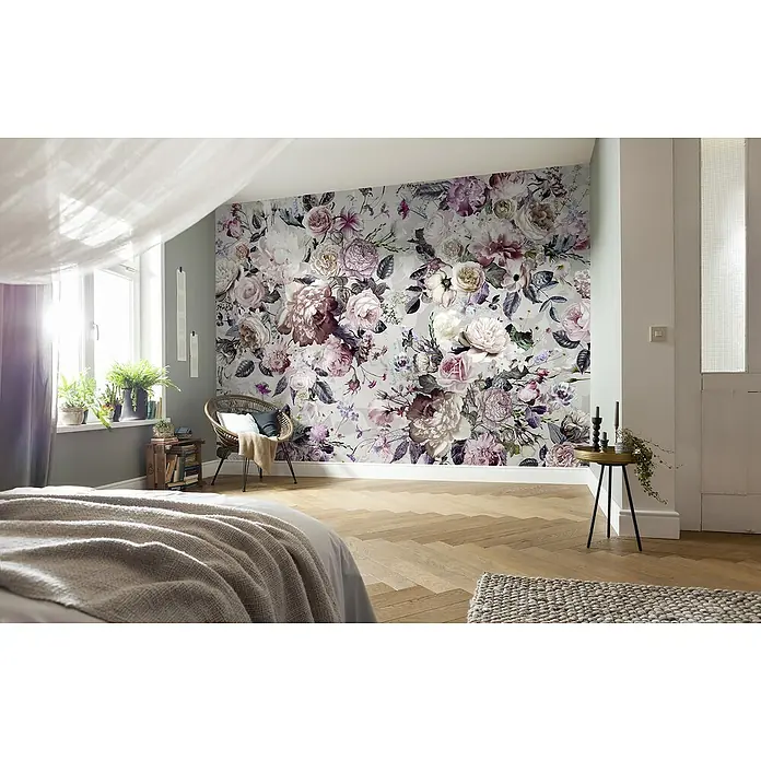 Komar Fototapete Blossoms - 7 -tlg., B x H: 350 x 250 cm, Vlies - Ein Schlafzimmer mit einer floralen Wandtapete in Lila- und Weißtönen, einem Rattansessel und einem hellen Holzboden, das eine gemütliche Atmosphäre bietet.