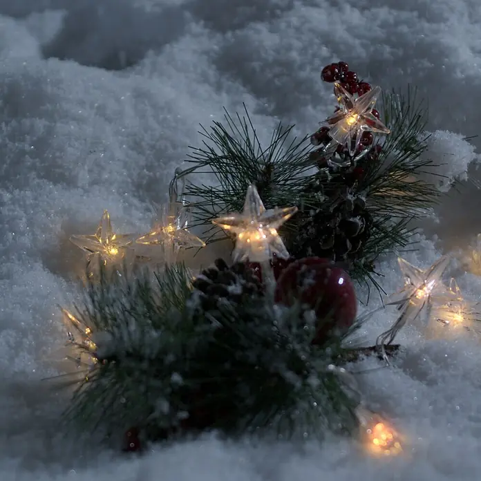 Konstsmide LED-Lichterkette Sterne - Außen, Lichtfarbe: Warmweiß, Anzahl Leuchtmittel: 40 Stk., Batteriebetrieben - Winterliche Szene mit funkelnder Sternenlichterkette, Tannenzweigen, Zapfen und roten Beeren im Schnee.