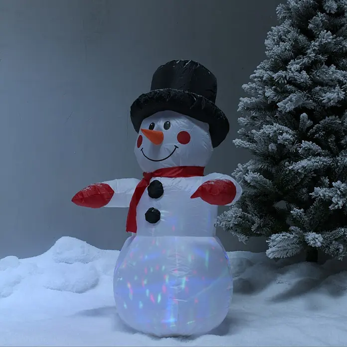 Figura LED navideña - Funcionamiento en red, LED - Un muñeco de nieve inflable con sombrero, bufanda roja y guantes está de pie en la nieve, iluminado por luces de colores. Figura decorativa de invierno.