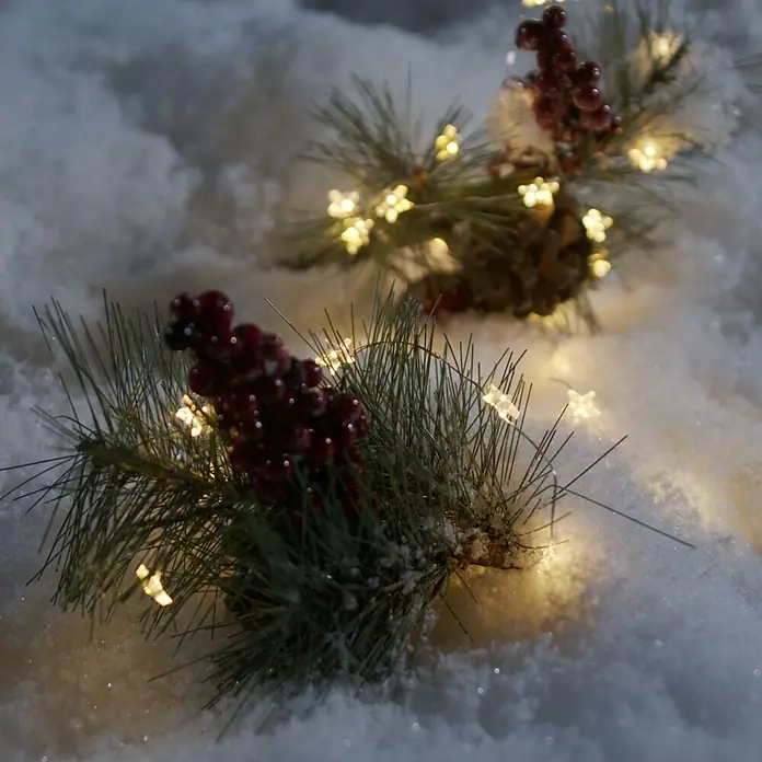 Konstsmide LED-Lichterkette Leuchtsterne - Innen, Lichtfarbe: Warmweiß, Anzahl Leuchtmittel: 40 Stk., Batteriebetrieben - Winterliche Szene mit Tannenzweigen, roten Beeren und Sternenlichtern im Schnee, die eine festliche Atmosphäre schaffen.