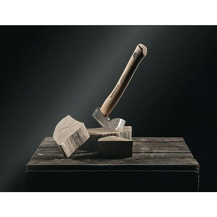 Jägerbeil-Set - 500 g, 330 mm - Eine Axt der Marke Swiss Made Jägerbeil steckt in einem Holzscheit auf einem rustikalen Holztisch, vor einem dunklen Hintergrund.