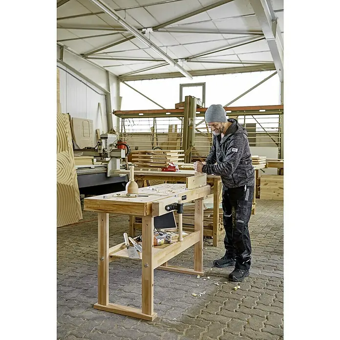 Ramia Hobelbank Advanced 1500 - L x B: 1.500 x 650 mm, Arbeitshöhe: 850 mm, Holz - Ein Handwerker arbeitet an einer Hobelbank in einer Werkstatt. Die Hobelbank ist aus hellem Holz gefertigt und bietet viel Stauraum.