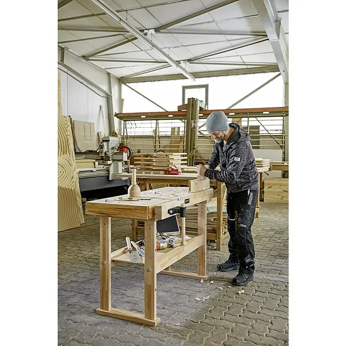 Ramia Hobelbank Advanced 1500 - L x B: 1.500 x 650 mm, Arbeitshöhe: 850 mm, Holz - Ein Handwerker arbeitet an einer Hobelbank in einer Werkstatt. Die Werkbank ist aus hellem Holz gefertigt und wirkt sehr robust.