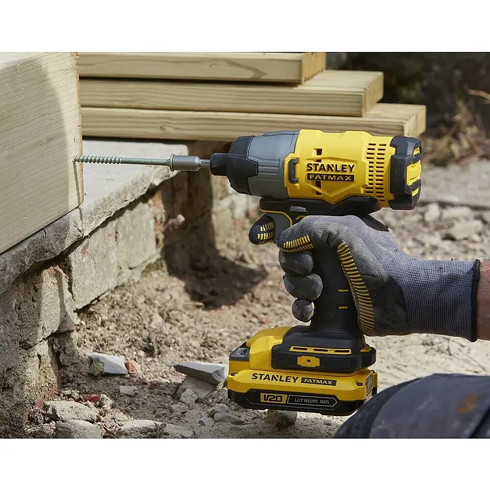 Stanley Fatmax V20 Taladro atornillador percutor de batería SFMCF800D1K - 18 V, 1 batería, 2 Ah, 165 Nm - El atornillador de impacto inalámbrico STANLEY FATMAX V20 se utiliza para atornillar un tornillo en un trozo de madera, que se encuentra junto a una pared de ladrillo.