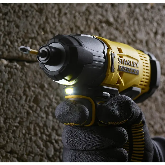 Stanley Fatmax V20 Taladro atornillador percutor de batería SFMCF800D1K - 18 V, 1 batería, 2 Ah, 165 Nm - Primer plano de un atornillador de impacto inalámbrico Stanley Fatmax amarillo y negro con la luz LED encendida, sostenido por una mano con un guante.