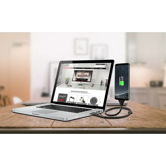 T'nB Cable USB - Largo: 60 cm, Conexión USB-C - El teléfono se está cargando mediante un cable USB robusto desde un ordenador portátil sobre una mesa de madera.
