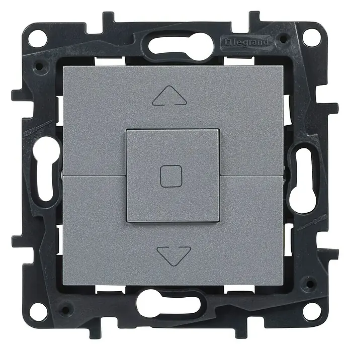 Legrand Niloé Step Interruptores para persianas - Aluminio, Mate, Montaje en superficie - Primer plano de un interruptor de luz Legrand gris con símbolos de flecha y cuadrado, en un marco negro texturizado.