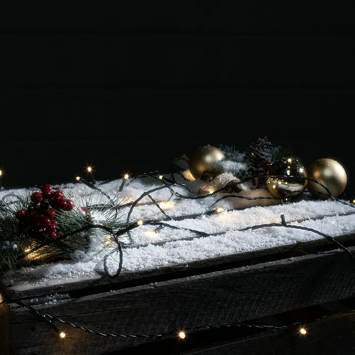 Tween Light LED-Lichterkette - Außen, Lichtfarbe: Warmweiß, Anzahl Leuchtmittel: 200 Stk., Netzbetrieben, 35 m - Festliche Szene mit glänzenden goldenen Kugeln, roten Beeren und warm leuchtenden Lichterketten auf einer Schneedecke, ideal für weihnachtliche Dekorationen.