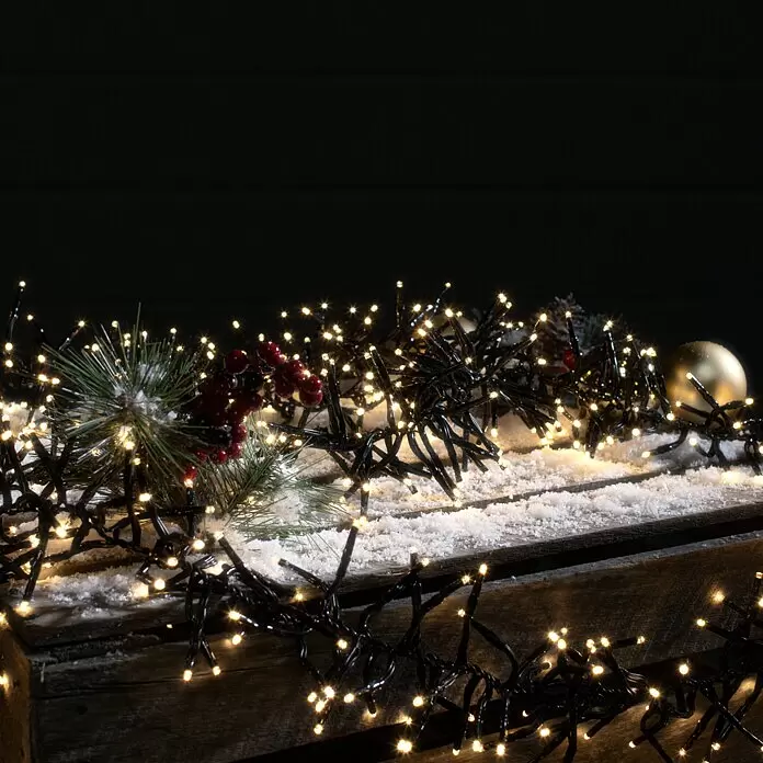 Tween Light LED-Clusterlichterkette - Außen, Länge: 12,4 m, 1.000 Stk., Netzbetrieben, Lichtfarbe: Warmweiß - Warmweiße LED-Lichterkette mit schwarzem Kabel auf einer verschneiten Holzkiste mit Tannengrün, Beeren und goldener Kugel.