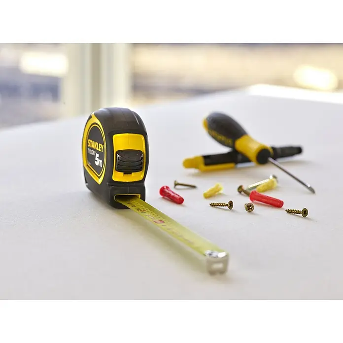 Stanley Cinta métrica extensible BIMATERIA TYLON™ - Largo: 5 m, Plástico - Primer plano de una cinta métrica Stanley junto con tornillos y destornilladores, sobre una superficie plana.