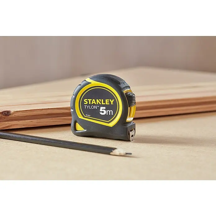 Stanley Cinta métrica extensible BIMATERIA TYLON™ - Largo: 5 m, Plástico - Cinta métrica Stanley Tylon 5m con lápiz sobre una mesa de madera. Una herramienta útil para mediciones precisas en proyectos de bricolaje y profesionales.