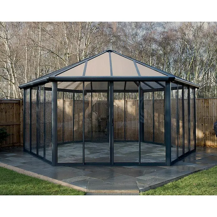 Palram – Canopia Pérgola de jardín cerrado Garda - L x An x Al: 5,95 x 5,17 x 3,13 m, Aluminio, Gris - La imagen muestra una moderna glorieta octogonal con paredes transparentes y un techo ligero, situada en un jardín.