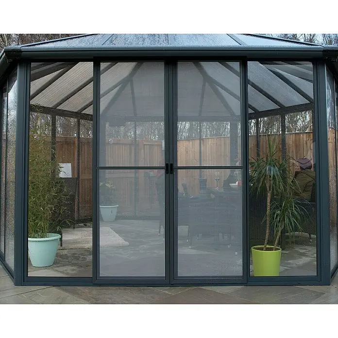 Palram – Canopia Pérgola de jardín cerrado Garda - L x An x Al: 5,95 x 5,17 x 3,13 m, Aluminio, Gris - La imagen muestra un invernadero detallado con plantas, destacando su arquitectura y paredes de vidrio.