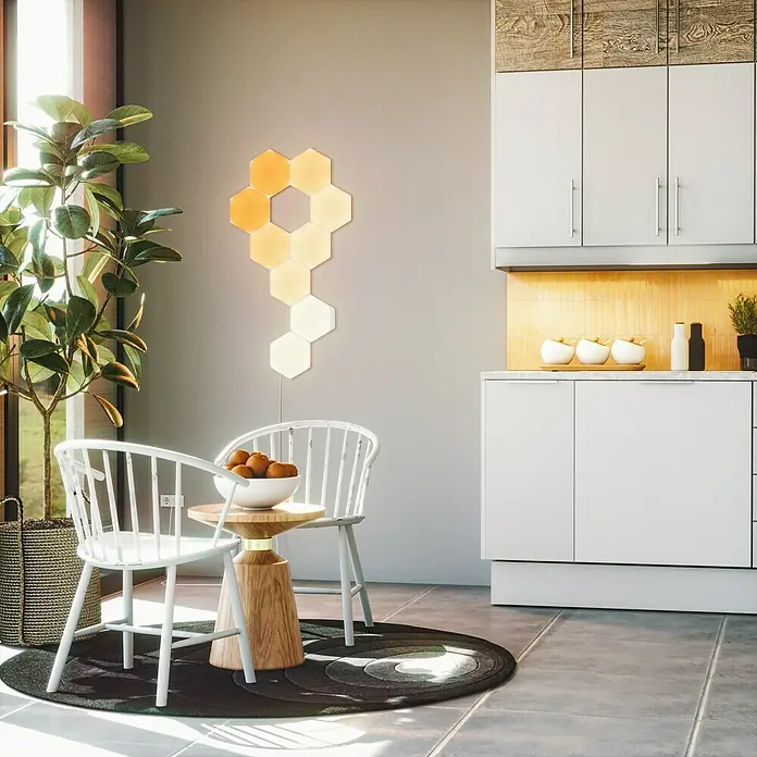 Nanoleaf Erweiterungskit Shapes Hexagons 3 Panels - 3 Stk., Weiß, RGBW, Hexagons, Smart Home-fähig: Ja - Stimmungsaufhellende Nanoleaf Light Panels an der Wand über einem Esstisch mit Obstschale, die das Ambiente des Raumes verbessern.