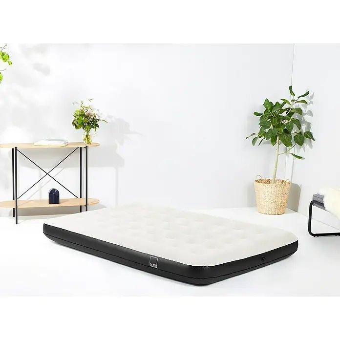 Luftbett Double - L x B x H: 191 x 137 x 22 cm, Schwarz/Grau - Eine Luftmatratze in einem hellen Raum, neben einem Beistelltisch und einer Pflanze. Die Matratze ist weiß mit einem schwarzen Rand.