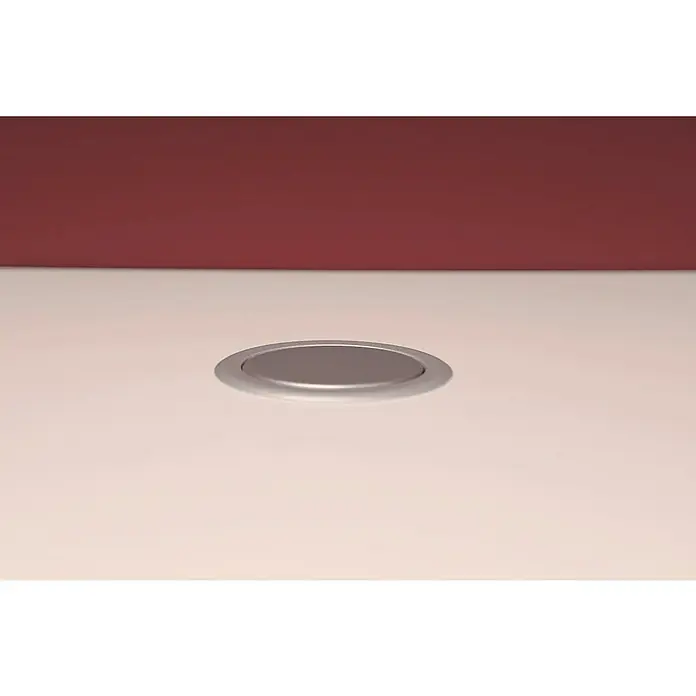 UniTEC Tischsteckdose - Versenkbar, Silber/Schwarz, 10,2 x 11 x 40 cm - Bündig montierter, runder, silberner Tischeinlass zur Kabeldurchführung auf beigem Tisch vor weinrotem Hintergrund.