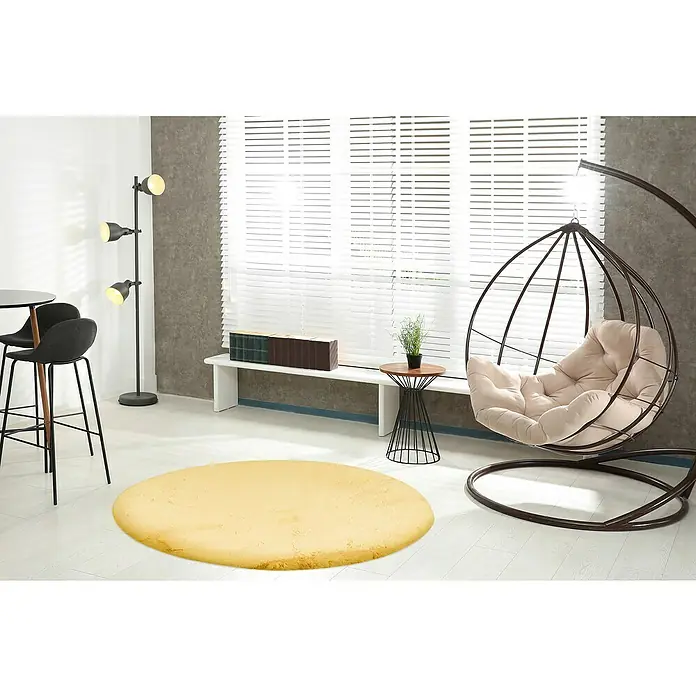 Fellteppich Happy - Gelb, Durchmesser: 120 cm, 100 % Polyester (Flor) - Ein gelber, runder Teppich liegt in einem modern eingerichteten Raum mit einem Hängesessel und minimalistischen Möbeln.