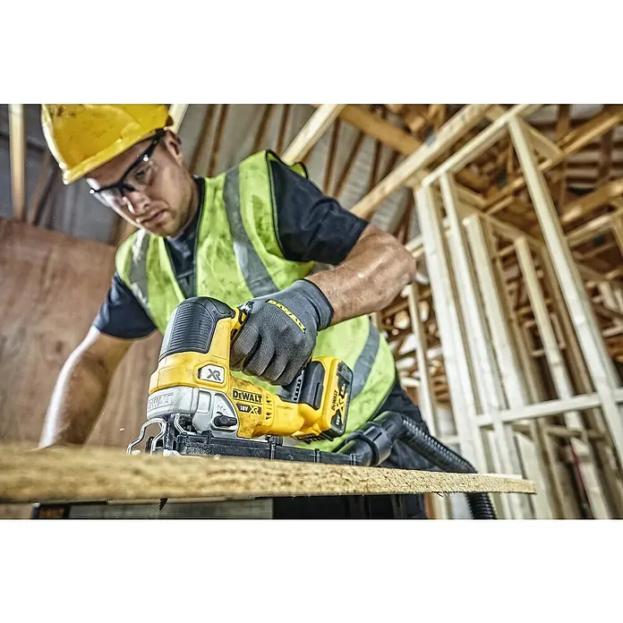 DeWalt XR 18V Sierra de calar a batería con acción pendular DCS334NT - 18 V, Sin batería, Número de carreras marcha en vacío: 3.200 /min - Un trabajador de la construcción con casco y gafas de seguridad utiliza una sierra de calar DeWalt amarilla para cortar un trozo de madera.
