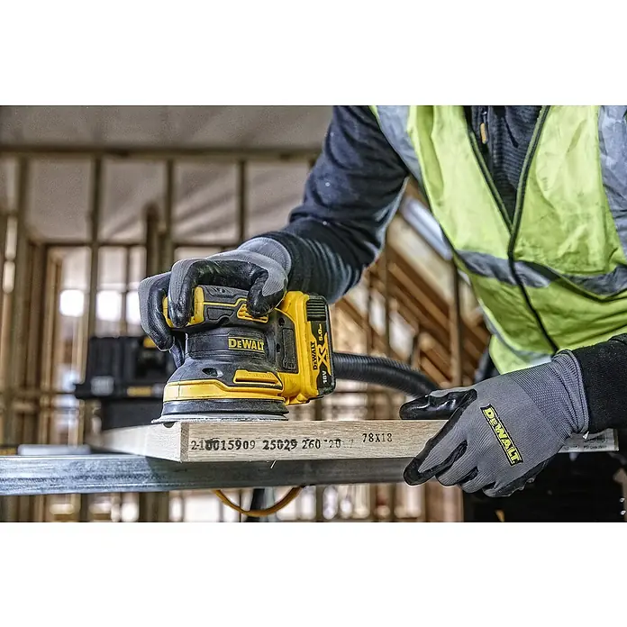 DeWalt XR 18V Akku-Exzenterschleifer DCW210N-XJ - 18 V, Ohne Akku, Durchmesser Schleifteller: 125 mm, Karton - Ein Arbeiter benutzt einen DeWalt-Schleifer, um ein Holzstück zu bearbeiten. Die gelbe Schleifmaschine ist mit einem Akku ausgestattet.