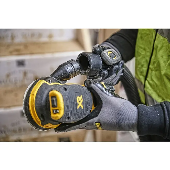 DeWalt XR 18V Akku-Exzenterschleifer DCW210N-XJ - 18 V, Ohne Akku, Durchmesser Schleifteller: 125 mm, Karton - Ein Dewalt-Exzenterschleifer wird an einen Staubsauger angeschlossen, um Staub zu entfernen und eine sauberere Arbeitsumgebung zu gewährleisten.