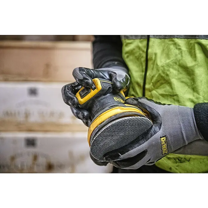 DeWalt XR 18V Akku-Exzenterschleifer DCW210N-XJ - 18 V, Ohne Akku, Durchmesser Schleifteller: 125 mm, Karton - Nahaufnahme eines DeWalt-Exzenterschleifers, der von behandschuhten Händen gehalten wird, ideal für Holzbearbeitung.